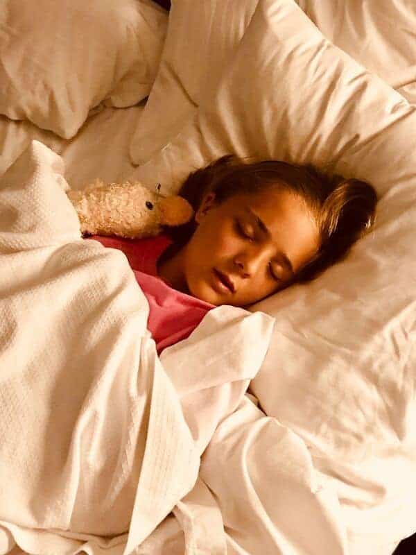 child-sleeping-white-sheets-with-doll