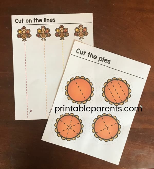 two printable Thanksgiving cutting practice worksheets on a wooden table. Text reads cut the pies and pictures four clip art pumpkin pies with lines to cut. Other worksheet says cut on the lines and has four turkeys with dotted lines to cut.